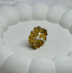 Gold leaf-patterned ring on a textured white surface