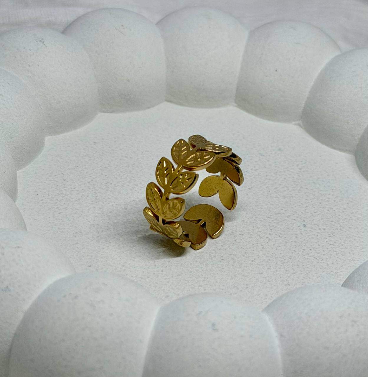 Gold leaf-patterned ring on a textured white surface